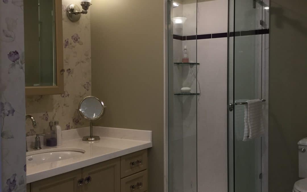 Bathroom interior featuring a modern vanity with a circular mirror, glass shower enclosure, and floral wallpaper, highlighting a renovation project by Profile Renovation in Langley, BC.