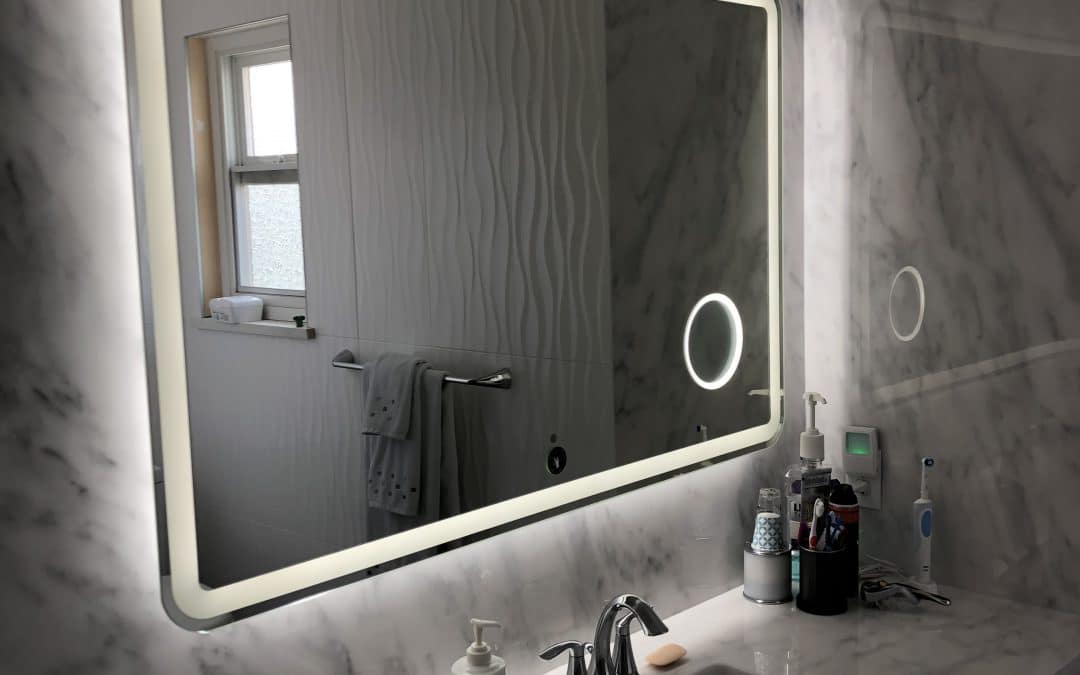 Modern bathroom with illuminated mirror, marble walls, and sink area featuring toiletries and a towel rack.