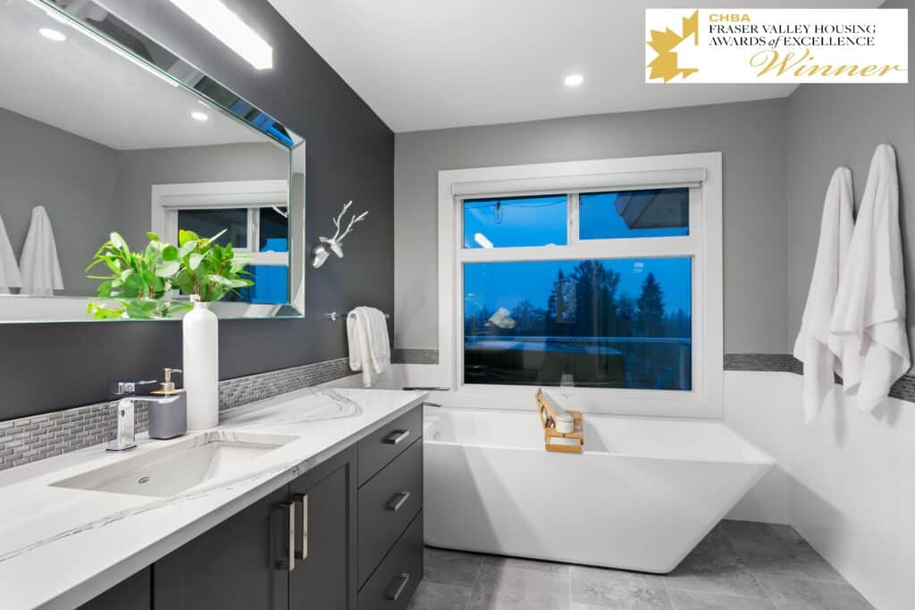 Modern bathroom design featuring a sleek vanity with dual sinks, a freestanding bathtub, large mirror, and contemporary fixtures, emphasizing functionality and aesthetic appeal, awarded CHBA Fraser Valley Housing Awards of Excellence.