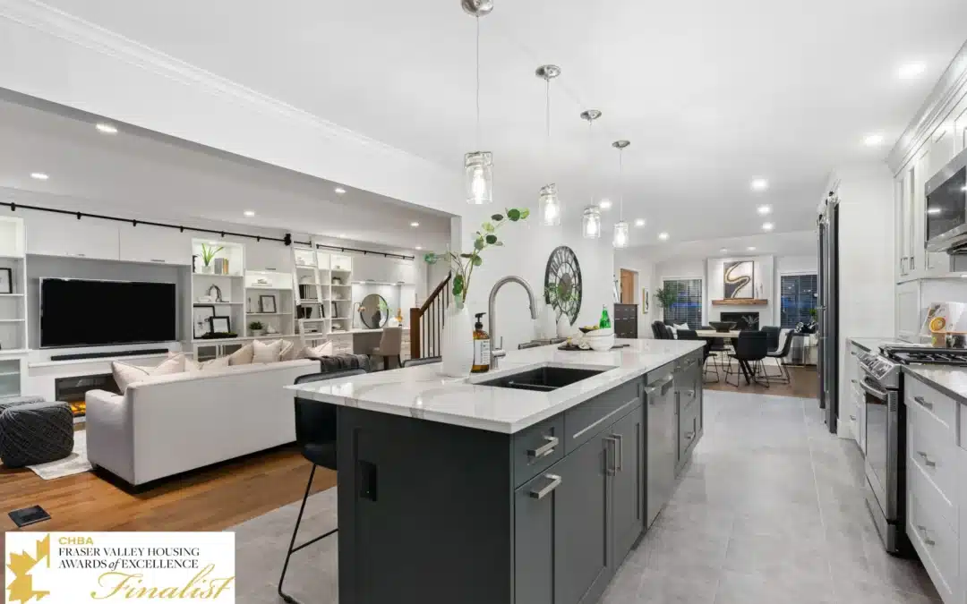 Modern kitchen interior featuring a central island with a dark gray cabinet, white countertop, and stainless steel appliances, complemented by a cozy living area with a white sofa and stylish decor, showcasing contemporary home renovation design.